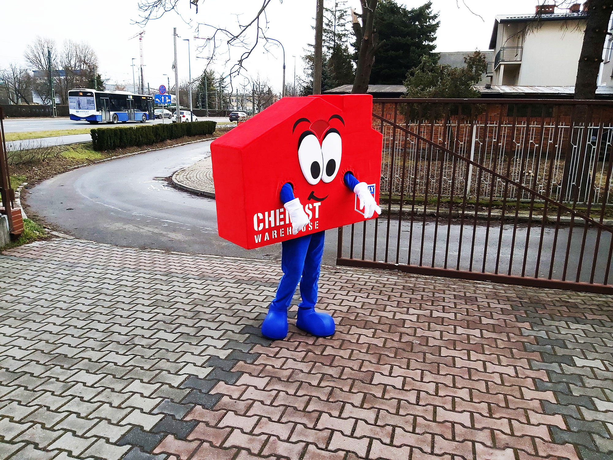 Na fotografii widnieje maskotka w postaci domu pozująca do zdjęcia w pobliżu siedziby firmy Elabika